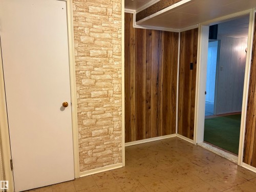 Interior space featuring wood-finish paneling, stone-look accent wall, and a solid white door - 5511 50 St, Tofield, AB 