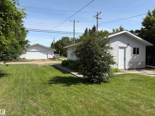 Expansive grassy yard area featuring two detached white structures with gabled roofs, siding exteriors, and concrete pads - 5511 50 St, Tofield, AB 