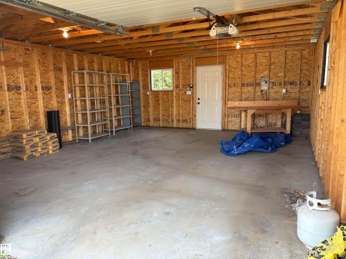 Spacious garage featuring exposed wood framing, a concrete floor, built-in workbench, and a garage door opener system - 5511 50 St, Tofield, AB 