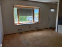 Spacious room with a large bay window featuring natural wood trim, white walls, and tan carpeting - 5511 50 St, Tofield, AB 