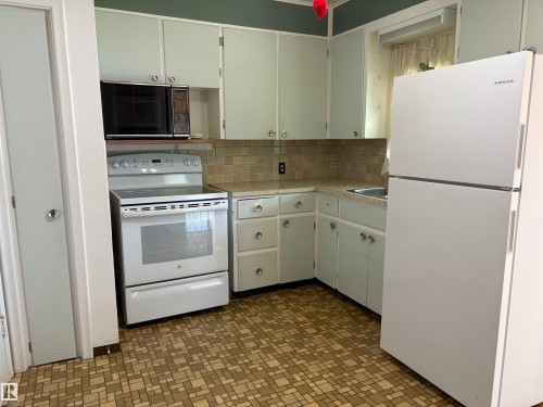 Kitchen featuring a white electric range, over-range microwave, and a white refrigerator - 5511 50 St, Tofield, AB 