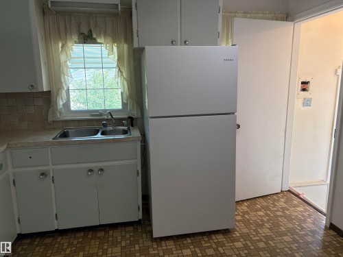 Kitchen featuring a white top-freezer refrigerator, dual-basin stainless steel sink, and white cabinetry - 5511 50 St, Tofield, AB 