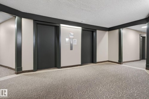 Building corridor featuring two elevators, textured carpet flooring, and a drop ceiling - 412 13910 Stony Plain Road, Edmonton, AB 