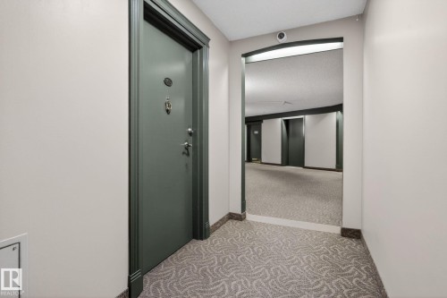 Entryway featuring a solid door with decorative hardware, a patterned carpet, and a marble baseboard - 412 13910 Stony Plain Road, Edmonton, AB 