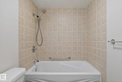 Bathroom tub and shower combination featuring neutral square wall tiles, chrome fixtures, and a white porcelain tub - 