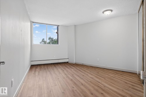 Bright room featuring a large window, wood-finish flooring, white painted walls, baseboard heating, and a flush-mount ceiling light - 412 13910 Stony Plain Road, Edmonton, AB 
