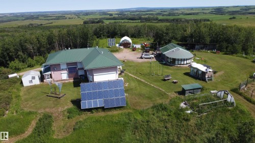 Expansive property featuring two distinct structures, multiple solar panel arrays, a greenhouse, and abundant green space, all surrounded by wooded areas - 55419 Rr73, Rural St. Paul County, AB 