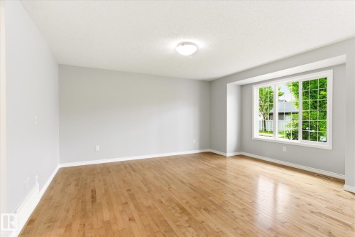 Spacious room featuring wood-finish flooring, light grey wall tones, and white trim - 9039 219 Street, Edmonton, AB 