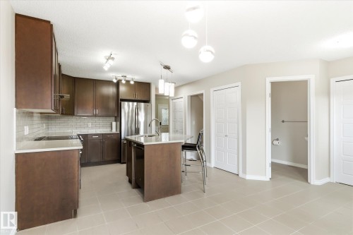 Modern kitchen featuring rich wood-finish cabinetry, white subway tile backsplash, stainless steel appliances, and a central island with a sink and pendant lighting - 9039 219 Street, Edmonton, AB 