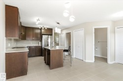 Modern kitchen featuring rich wood-finish cabinetry, white subway tile backsplash, stainless steel appliances, and a central island with a sink and pendant lighting - 