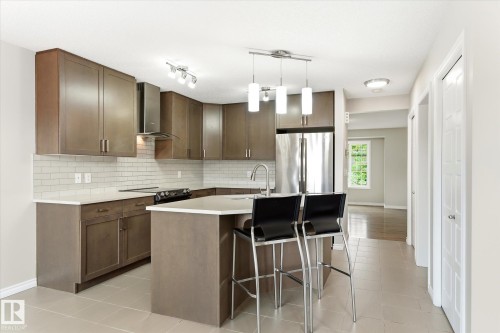 Modern kitchen featuring sleek stainless steel appliances, dark wood-finish cabinetry, a white subway tile backsplash, and an island with a breakfast bar - 9039 219 Street, Edmonton, AB 