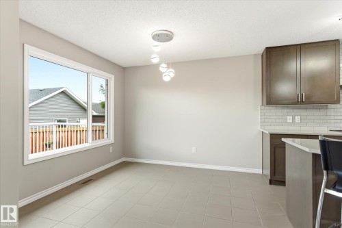 Open-concept living space with large window, tile flooring, contemporary pendant lighting, and kitchen island with seating - 9039 219 Street, Edmonton, AB 