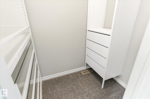 Custom closet organization system featuring white shelving, built-in drawers, gray carpet flooring, and white baseboard trim - 9039 219 Street, Edmonton, AB 