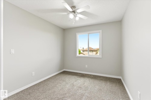 Neutral-toned room featuring a ceiling fan with integrated lighting, a window with a white frame, and gray carpeting - 9039 219 Street, Edmonton, AB 