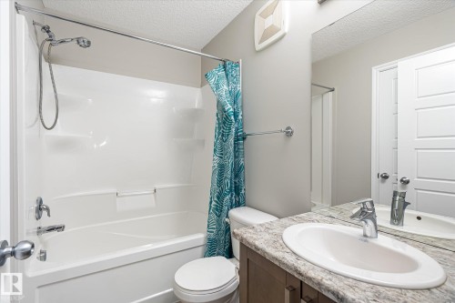 Bathroom featuring a white bathtub and shower combination with chrome fixtures, a vanity with a light-toned patterned countertop and integrated sink, a large wall-mounted mirror, and a white toilet - 9039 219 Street, Edmonton, AB 