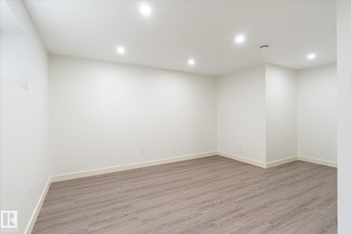 Spacious room featuring light wood-finish flooring, recessed ceiling lighting, and neutral wall tones - 9039 219 Street, Edmonton, AB 