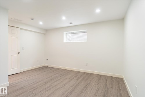 Spacious room featuring wood-finish flooring, recessed lighting, a white paneled door, a horizontal window with blinds, and white baseboards - 9039 219 Street, Edmonton, AB 