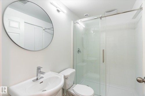 Contemporary bathroom featuring a pedestal sink with chrome faucet, circular wall mirror, and a glass-enclosed shower with white subway tile surround and a built-in shower niche - 9039 219 Street, Edmonton, AB 