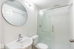 Contemporary bathroom featuring a pedestal sink with chrome faucet, circular wall mirror, and a glass-enclosed shower with white subway tile surround and a built-in shower niche - 