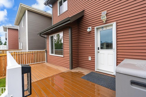 Wood-finish composite deck with white railings and privacy fencing, featuring a rear entry door with an integrated window, and a wall-mounted light fixture - 9039 219 Street, Edmonton, AB 