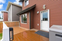 Wood-finish composite deck with white railings and privacy fencing, featuring a rear entry door with an integrated window, and a wall-mounted light fixture - 