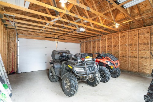 Spacious garage featuring exposed wood beam ceiling, concrete flooring, and a large white sectional garage door - 9039 219 Street, Edmonton, AB 