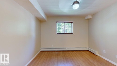 Room featuring a single window with blinds, wood-finish flooring, and baseboard heating - 201 11408 108 Avenue, Edmonton, AB 