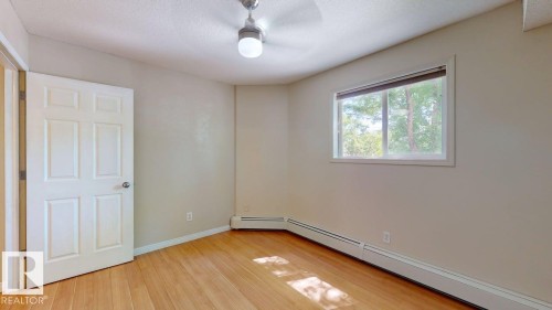 Room featuring light wood-finish flooring, a white six-panel door, and a single window with a white frame - 201 11408 108 Avenue, Edmonton, AB 