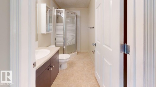 Bathroom featuring a shower enclosure with frosted glass, a vanity with a white countertop and wood-finish cabinetry, and a wall-mounted medicine cabinet - 201 11408 108 Avenue, Edmonton, AB 