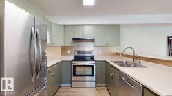 Kitchen featuring stainless steel appliances, light green cabinetry, wood-finish flooring, and a double basin sink with a gooseneck faucet - 
