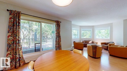 Open-concept living area featuring wood-finish flooring, a contemporary ceiling light fixture, and a bay window configuration - 201 11408 108 Avenue, Edmonton, AB 