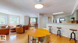 Open-concept living area featuring wood-finish flooring, multiple windows, a kitchen with light green cabinetry, stainless steel appliances, and a breakfast bar with built-in seating - 