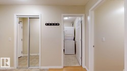 Hallway featuring a mirrored closet, wood-finish flooring, and a laundry area with stacked appliances - 