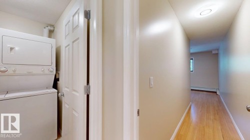 Dedicated laundry area featuring a stacked washer and dryer, complemented by a light wood-finish floor extending into the hallway - 201 11408 108 Avenue, Edmonton, AB 