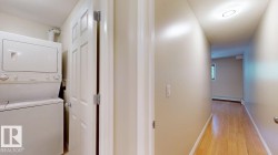Dedicated laundry area featuring a stacked washer and dryer, complemented by a light wood-finish floor extending into the hallway - 