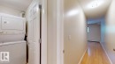 Dedicated laundry area featuring a stacked washer and dryer, complemented by a light wood-finish floor extending into the hallway - 201 11408 108 Avenue, Edmonton, AB 