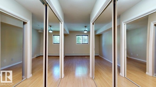 Bedroom featuring light wood-finish flooring, neutral wall tones, two windows with exterior views, and a ceiling fan with integrated lighting - 201 11408 108 Avenue, Edmonton, AB 
