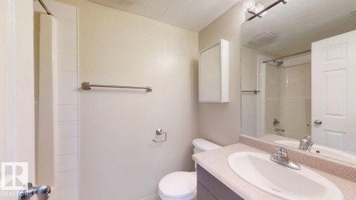 Bathroom featuring a shower-tub combination, single vanity with integrated sink, stone-look countertop, and a wall-mounted medicine cabinet - 201 11408 108 Avenue, Edmonton, AB 
