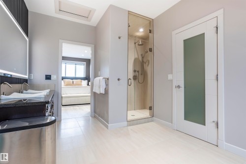 Contemporary bathroom featuring a glass-enclosed shower, dual vessel sinks on a dark countertop, an illuminated vanity mirror, and light tile flooring - 4949 Terwillegar Common, Edmonton, AB 