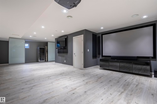 Entertainment space featuring a large projection screen, built-in media console, wood-finish flooring, recessed lighting, and sliding frosted glass panels - 4949 Terwillegar Common, Edmonton, AB 