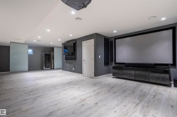 Entertainment space featuring a large projection screen, built-in media console, wood-finish flooring, recessed lighting, and sliding frosted glass panels - 