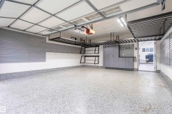 Spacious garage featuring a speckled epoxy floor, overhead storage racks, integrated slatwall panels, built-in cabinetry, and LED lighting - 