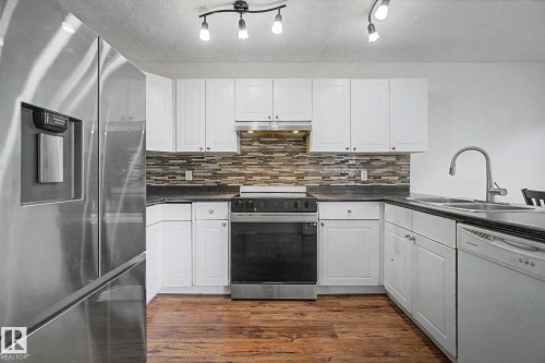 Kitchen featuring white shaker cabinetry, stainless steel appliances, dark countertops, and wood-finish flooring - 710 Glenwright Court, Edmonton, AB 