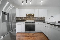 Kitchen featuring white shaker cabinetry, stainless steel appliances, dark countertops, and wood-finish flooring - 