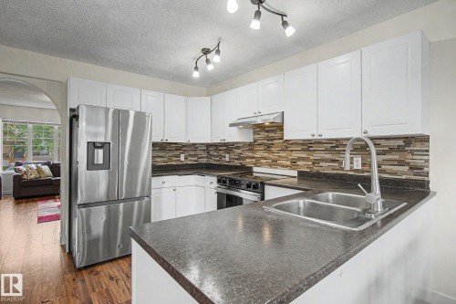 Modern kitchen featuring white cabinetry, stainless steel appliances, a dual basin sink, and a multi-tone tile backsplash - 710 Glenwright Court, Edmonton, AB 