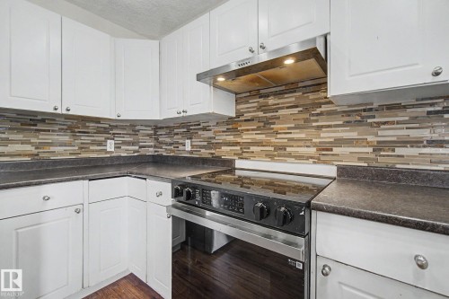 Kitchen featuring white cabinetry, dark countertops, a mosaic tile backsplash, stainless steel range hood, and a black and stainless steel range - 710 Glenwright Court, Edmonton, AB 
