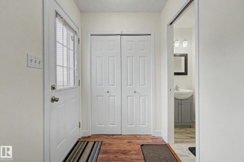 Entryway featuring wood-finish flooring, a white paneled door with an integrated window, bi-fold closet doors, and light-colored walls - 710 Glenwright Court, Edmonton, AB 