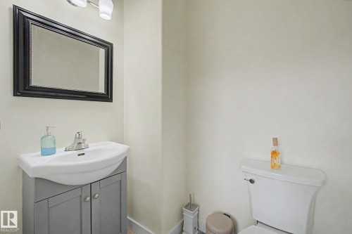 Bathroom featuring a wall-mounted vanity with integrated sink, chrome faucet, and a framed mirror with overhead lighting - 710 Glenwright Court, Edmonton, AB 