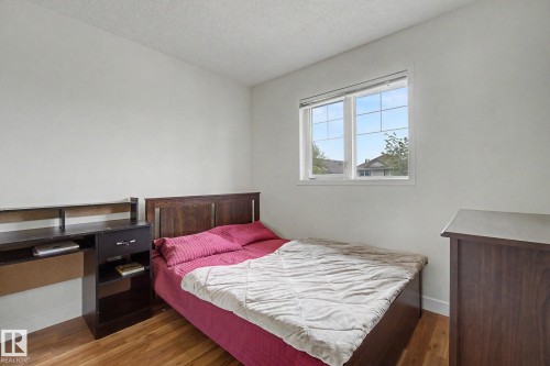Bedroom featuring wood-finish flooring, white walls, and a large window with grid-patterned panes - 710 Glenwright Court, Edmonton, AB 