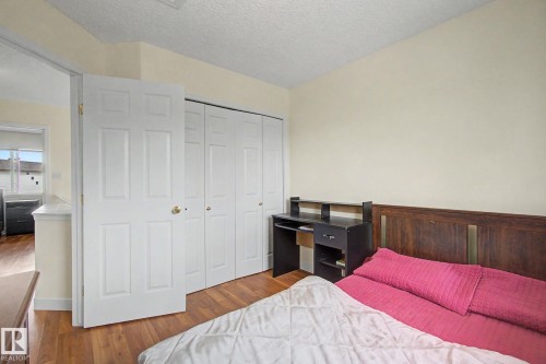 Interior room featuring wood-finish flooring, a six-panel door, and a wall of bi-fold closet doors - 710 Glenwright Court, Edmonton, AB 